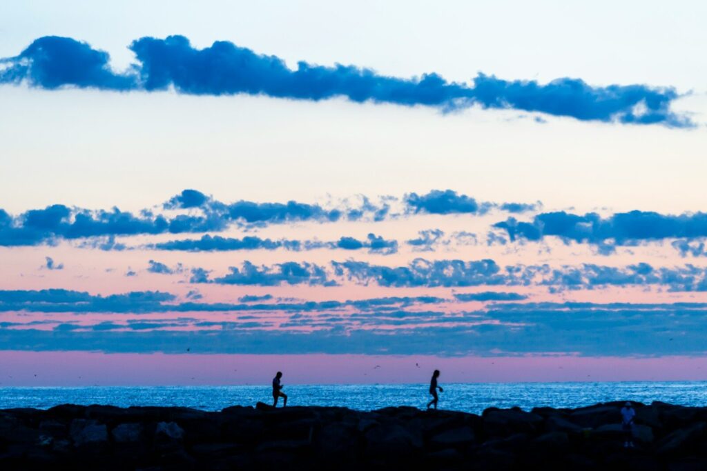 People walk along the ocean at sunset.